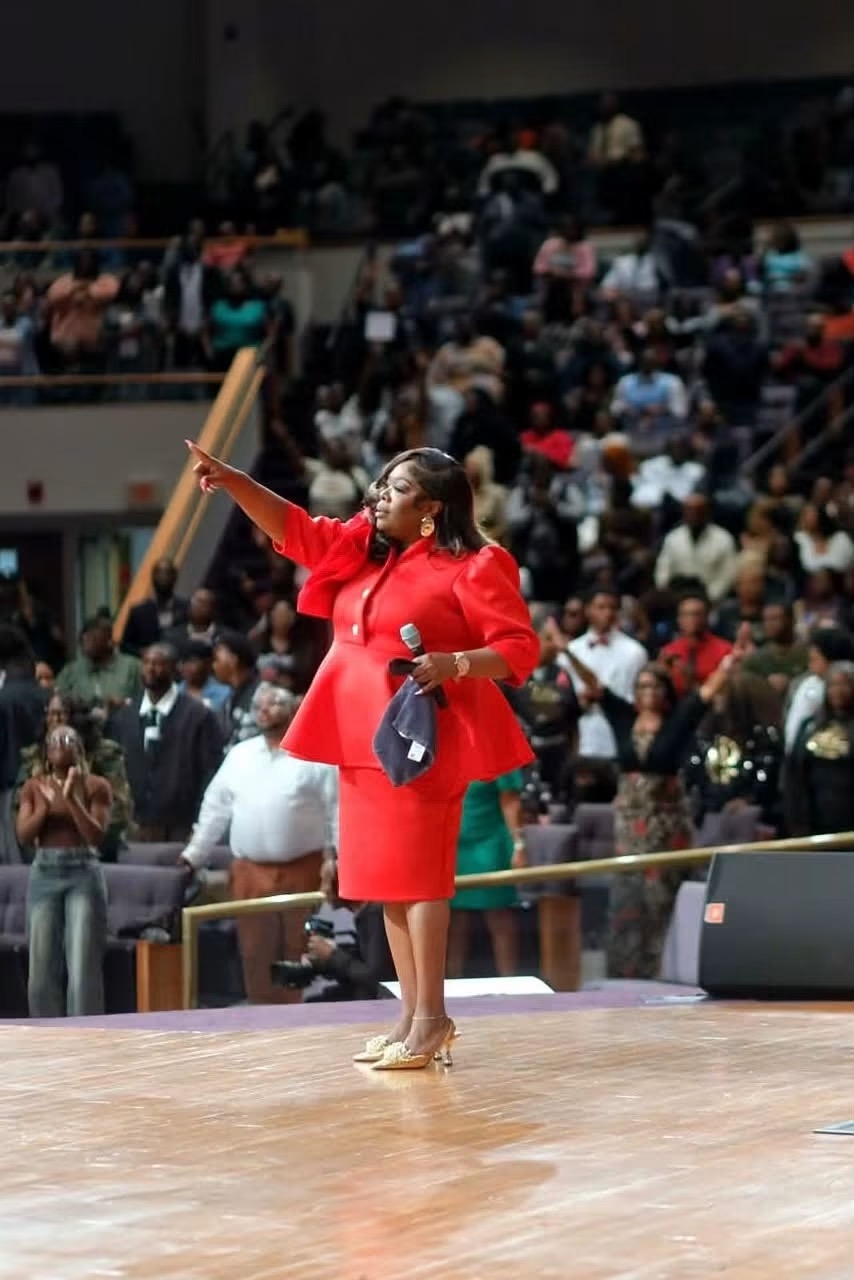 Amelia in a red dress leading a gospel gathering from the stage